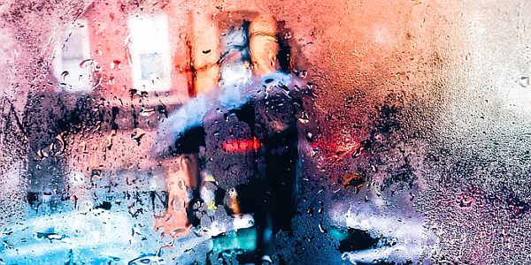 person holding umbrella seen through window with droplets on it