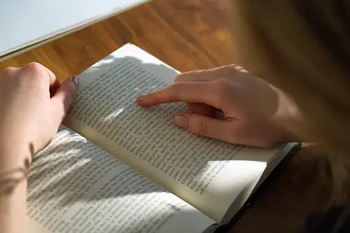 Sunlight falling on a person reading a book while moving their finger along the lines.